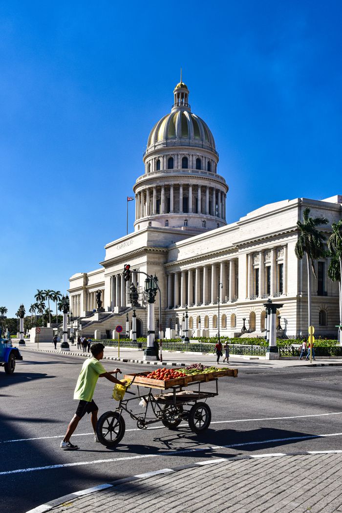 about-us-02 Street vendor with fruit cart in front of Havana's Capitol Building under a clear blue sky.